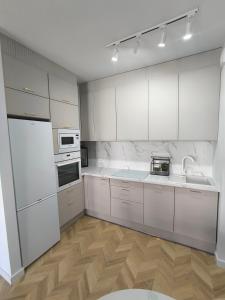 a white kitchen with white appliances and wooden floors at Apartamenty Sady in Słubice +18 photos