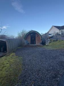 a brick house with a door on a gravel driveway at Woodside Round Pod in Fort William