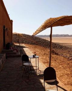 a table with chairs and an umbrella in the desert at Riad Nomad in Foum Mharech