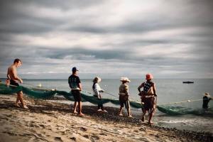 a group of people standing on the beach with a boat at Caba La Union Gulfside Cottage C3 in Caba +5 photos