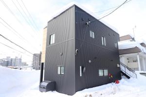 a black building with snow on the ground at Cloud House Sapporo in Sapporo
