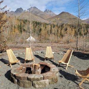 three chairs and a fire pit with mountains in the background at Alaskan Glamping in Anchorage