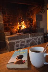 a book and a cup of coffee on a table with a fireplace at gîte La Maison d'Odette in Saint-Rémy-du-Plein