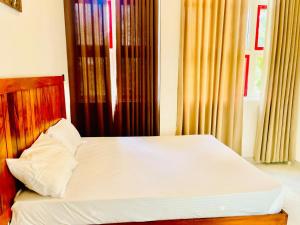 a bedroom with a bed with a wooden headboard and curtains at Green Crown Villa in Polonnaruwa +4 photos