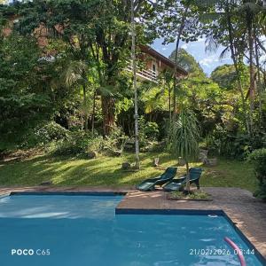 a swimming pool with two chairs and a house at Refúgio Pasárgada Guest House in Mairiporã +69 photos