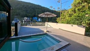 a swimming pool with an umbrella next to a house at Loft com piscina, sauna e hidro in Niterói