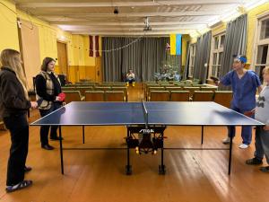 a group of people standing around a ping pong table at Rozulas skola in Rozula