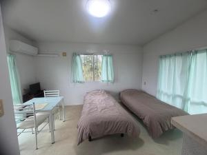 a bedroom with two beds and a desk and a window at バケーションレンタル栄 in Ibaruma