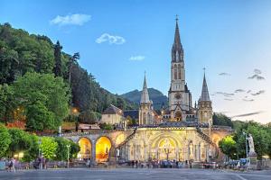 a large building with a church with a clock tower at Hôtel Myosotis in Lourdes