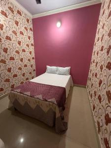 a small bed in a room with a purple wall at Karuna Homestay in Ujjain