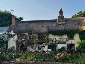 an old cottage with flowers in front of it at Honey Meadow Retreat in Ashreigney