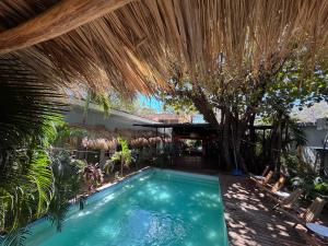 an outdoor swimming pool with a straw umbrella and trees at Refugio Surf Lodge in Tamarindo