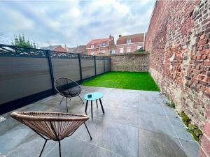 a patio with two chairs and a table and a brick wall at Plain-pied accès facile idéal séjour tranquille in Bailleul