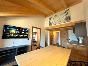 a dining room with a wooden table and a flat screen tv at Dolomiti Panorama - 3 Rooms in Carano