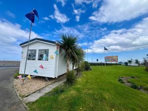 a small white house with a palm tree in a field at Seaside Caravan in a Leisure Park with WiFi & Parking - 3 bedrooms in Meliden