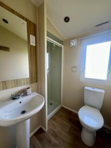a bathroom with a sink and a toilet and a mirror at Seaside Caravan in a Leisure Park with WiFi & Parking - 3 bedrooms in Meliden +8 photos
