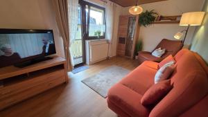 a living room with an orange couch and a flat screen tv at Kleines Glück am Bärenstein in Gößweinstein