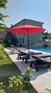a picnic table with a red umbrella next to a pool at La Maison d'ART in Lacour
