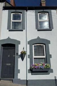 a white house with two windows and a door and flowers at Derry City Centre Townhouse in Derry Londonderry
