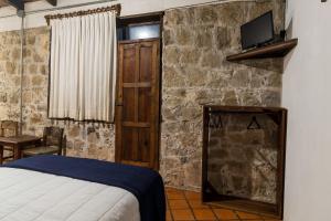 a bedroom with a bed and a tv on a stone wall at Casa Huitsiki in Cuetzalán del Progreso