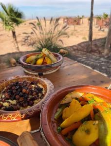 a wooden table with plates of food and a bowl of fruit at Be Nomad Agafay Camp in El Karia