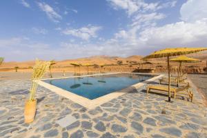 a swimming pool with chairs and umbrellas in the desert at Be Nomad Agafay Camp in El Karia