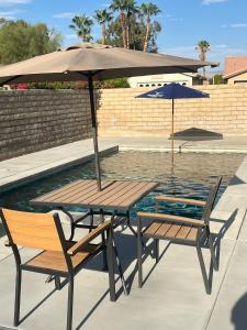 a table and two chairs with an umbrella next to a pool at Walking Distance to Stagecoach in Indio