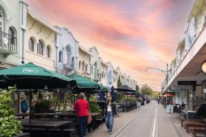 people walking down a street with tables and umbrellas at Quest Cathedral Junction Serviced Apartments in Christchurch