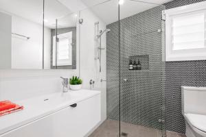 a white bathroom with a shower and a sink at The Treehouse Avalon in Whale Beach
