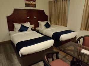 two beds in a hotel room with a glass table at Hotel Gentleman Mithila in Eramalloor