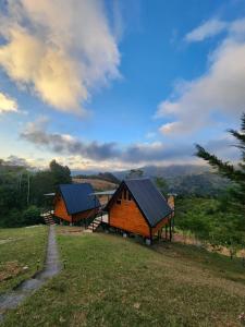 two wooden cabins with blue roofs on a field at Brisas De Los Santos Lodge 1 in Sierra