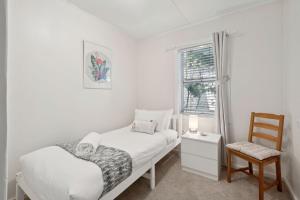 a white bedroom with a bed and a chair at Misty Pines in Leura
