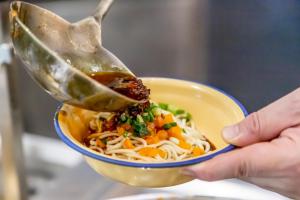a person holding a bowl of noodles with a spoon at Shangri-La Wuhan, Interchange hub of three metro lines,Adjacent to the MixC in Wuhan