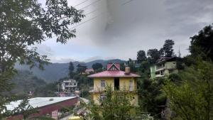 a yellow house on a hill with mountains in the background at Suket homestay in Jhungi