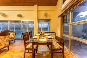 a dining room with a table and chairs and windows at Gauri Villa by ELIVAAS With Pool, Lounge, Garden & Bathtub With 360 Panoramic Hill Views Near Waterfalls in Kasāra