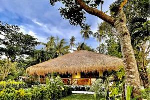 a hut with a thatched roof and a palm tree at Sunset at Las Cabanas in El Nido