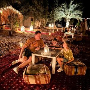a man and two children sitting at a table with a candle at Overnight Luxury Camp in Merzouga