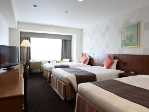 a hotel room with three beds and a flat screen tv at Loisir Hotel Toyohashi in Toyohashi