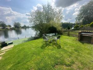 a table and chairs in the grass next to a river at Lakeside Retreat 3 with hot tub, private fishing peg situated at Tattershall Lakes Country Park in Tattershall