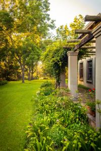 a garden next to a white house with trees at The River Villa in Magaliesburg