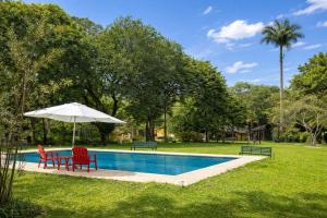 a pool with two red chairs and an umbrella at Sítio Mais Lindo do Mundo in Ilha de Guaratiba