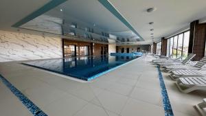 a large swimming pool in a building with white chairs at Sand & Wave - Luxury Marina View Apartment with Spa, Pool & Free Parking in Dziwnów