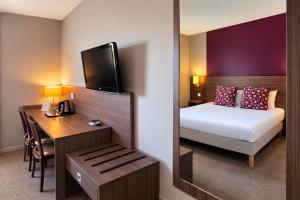 a hotel room with a bed and a desk and a mirror at The Originals City, Hôtel Les Bruyères, Dax Nord in Castets