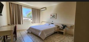 a bedroom with a bed and a desk and a window at Quarto Hotel Palhano londrina in Londrina