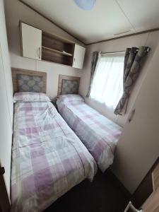 two beds in a small room with a window at Dornoch Holiday Chalet in Proncy