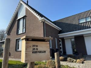 a house with a wooden sign in front of it at Kustgeluk-Luxe aan Zee, splinternieuw appartement in het hart van Koudekerke in Koudekerke