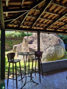a table and two stools in front of a rock at Wood house casa privada in Abraão +16 photos