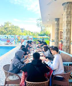 a group of people sitting at a long table near a pool at mountain Luxor in Al Aqālitah