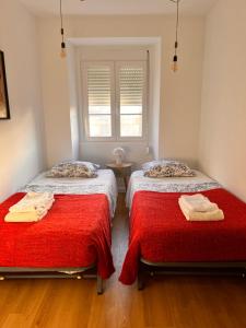 a bedroom with two beds with red sheets and a window at Sintra Central Apartment in Sintra