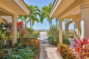 a walkway through a resort with palm trees and flowers at 3B Beachfront Condo - Heated Pool & 18ft Balcony in Holmes Beach